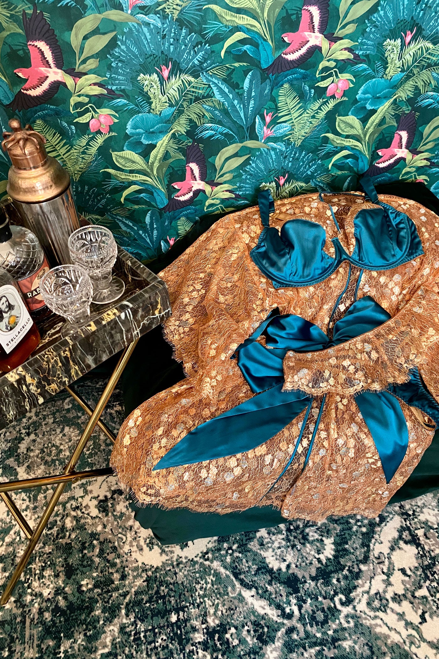 Gold lace robe with matching bra and thong flatlay with lush wallpaper and cocktails