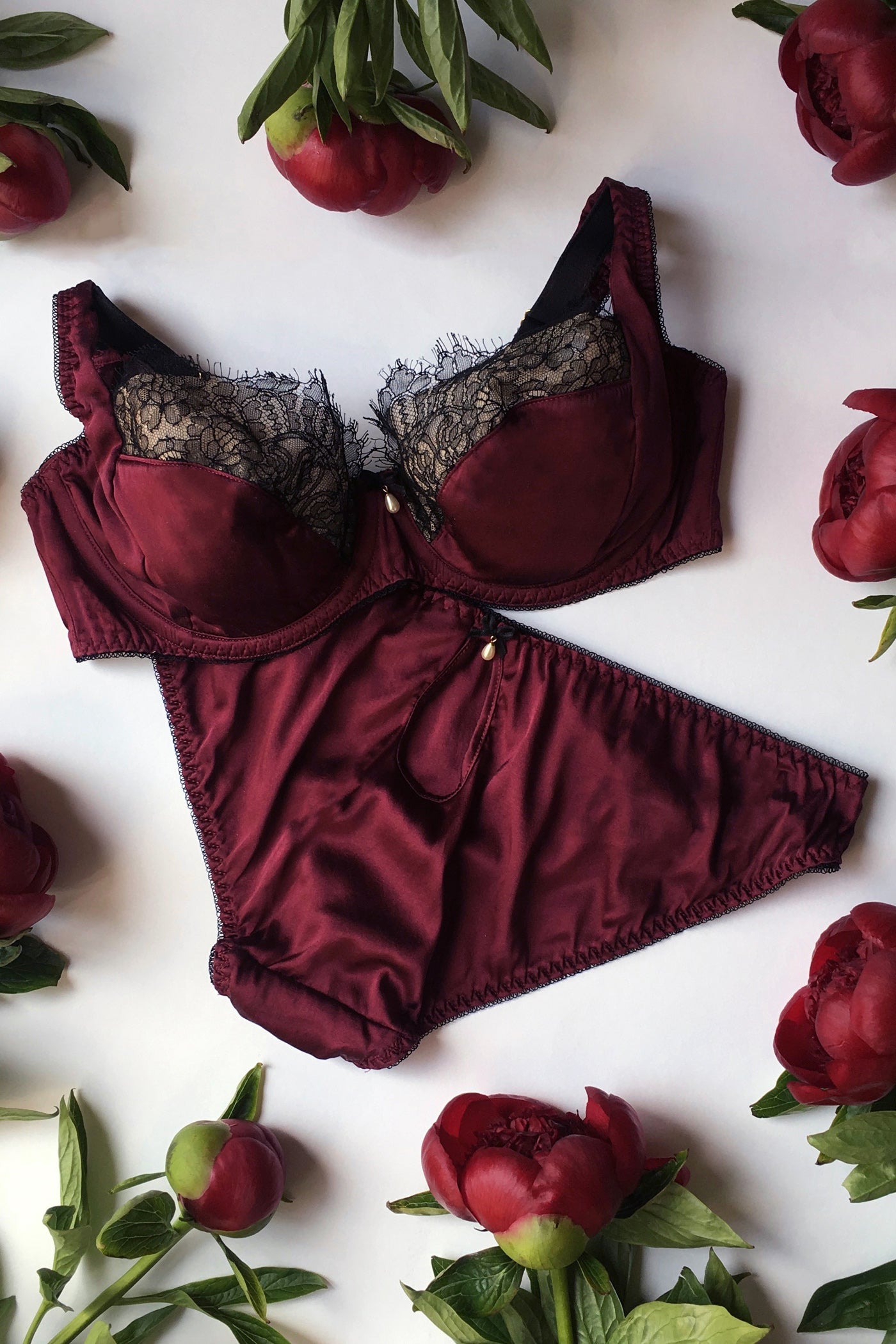 Silk and lace bra and panty in dark red silk and black lace flatlay, with pearl detail on both
