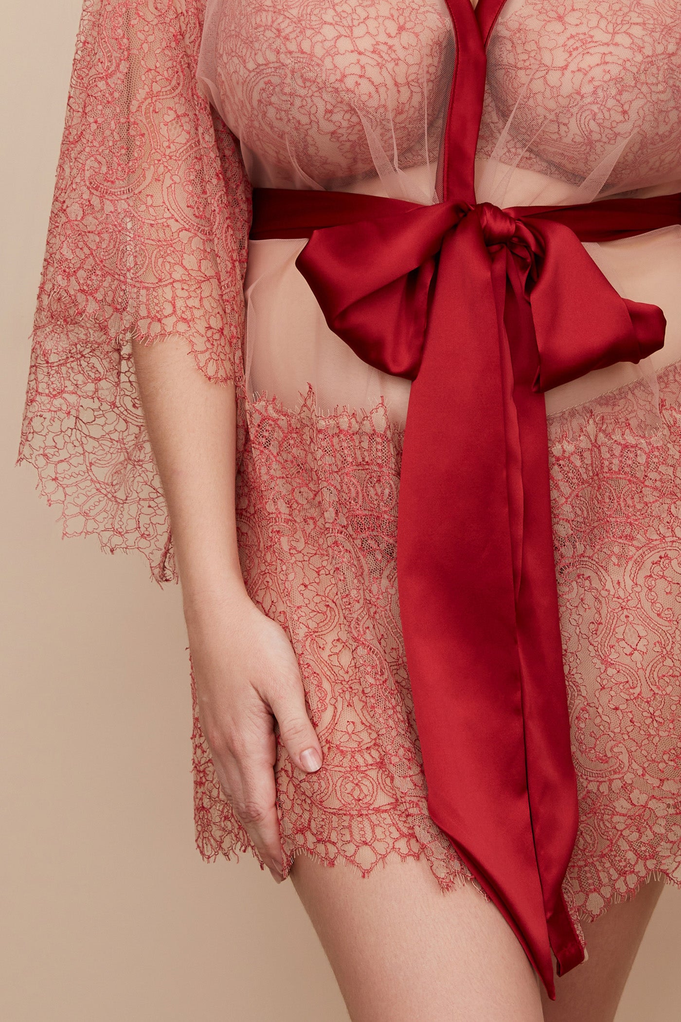 Closeup of red silk sash tied in bow and deep bands of fine french lace on robe