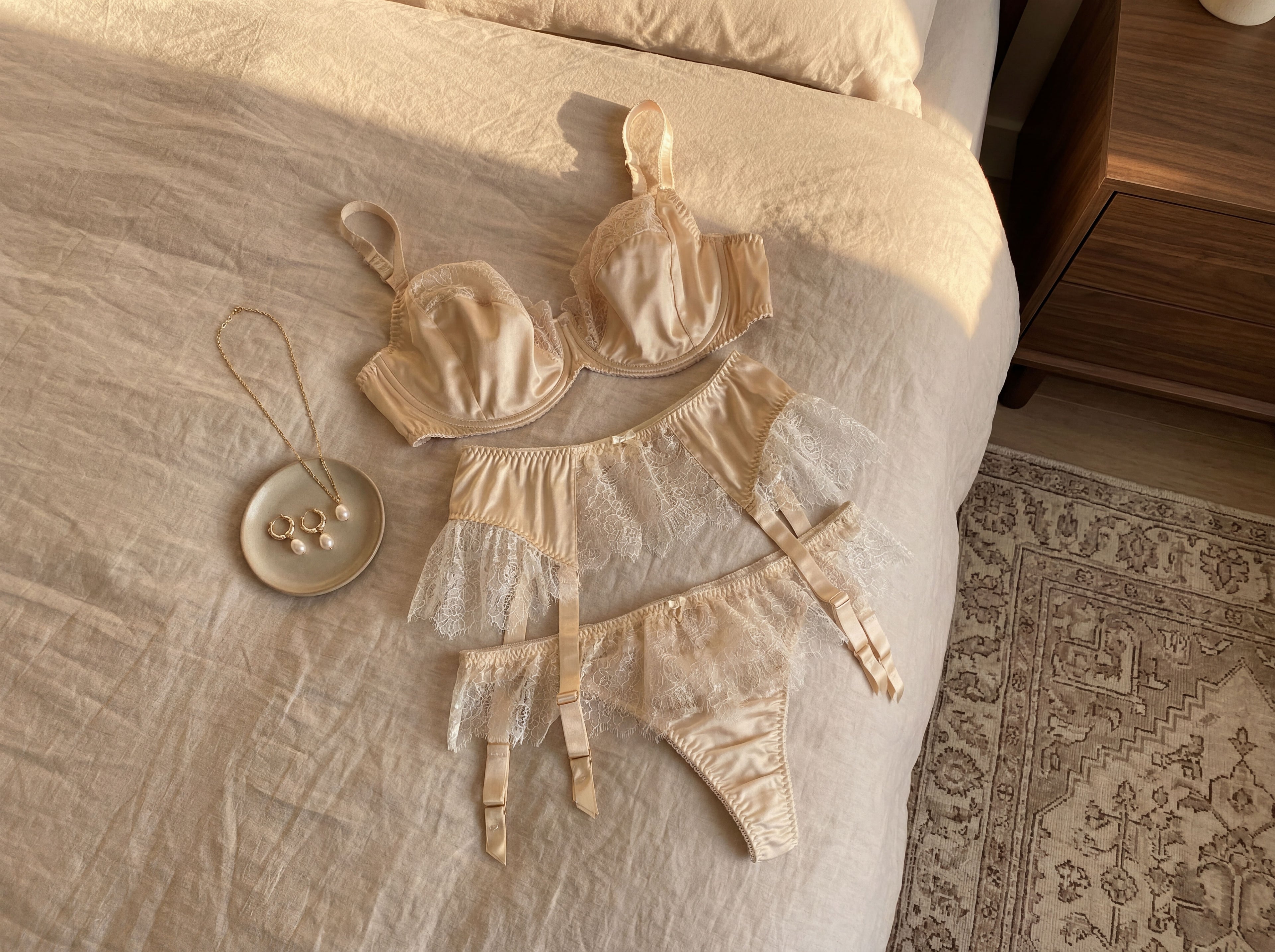 Cream silk and lace bra, suspender and thong on a bed with pearl jewellery 