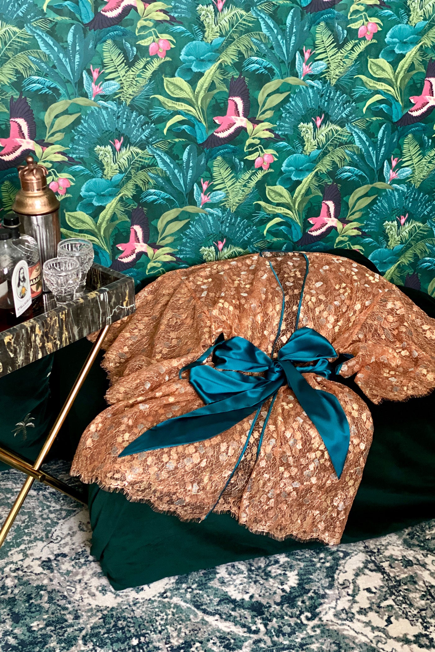 Metallic gold lace robe with turquoise silk sash flatlay against lush wallpaper and cocktails
