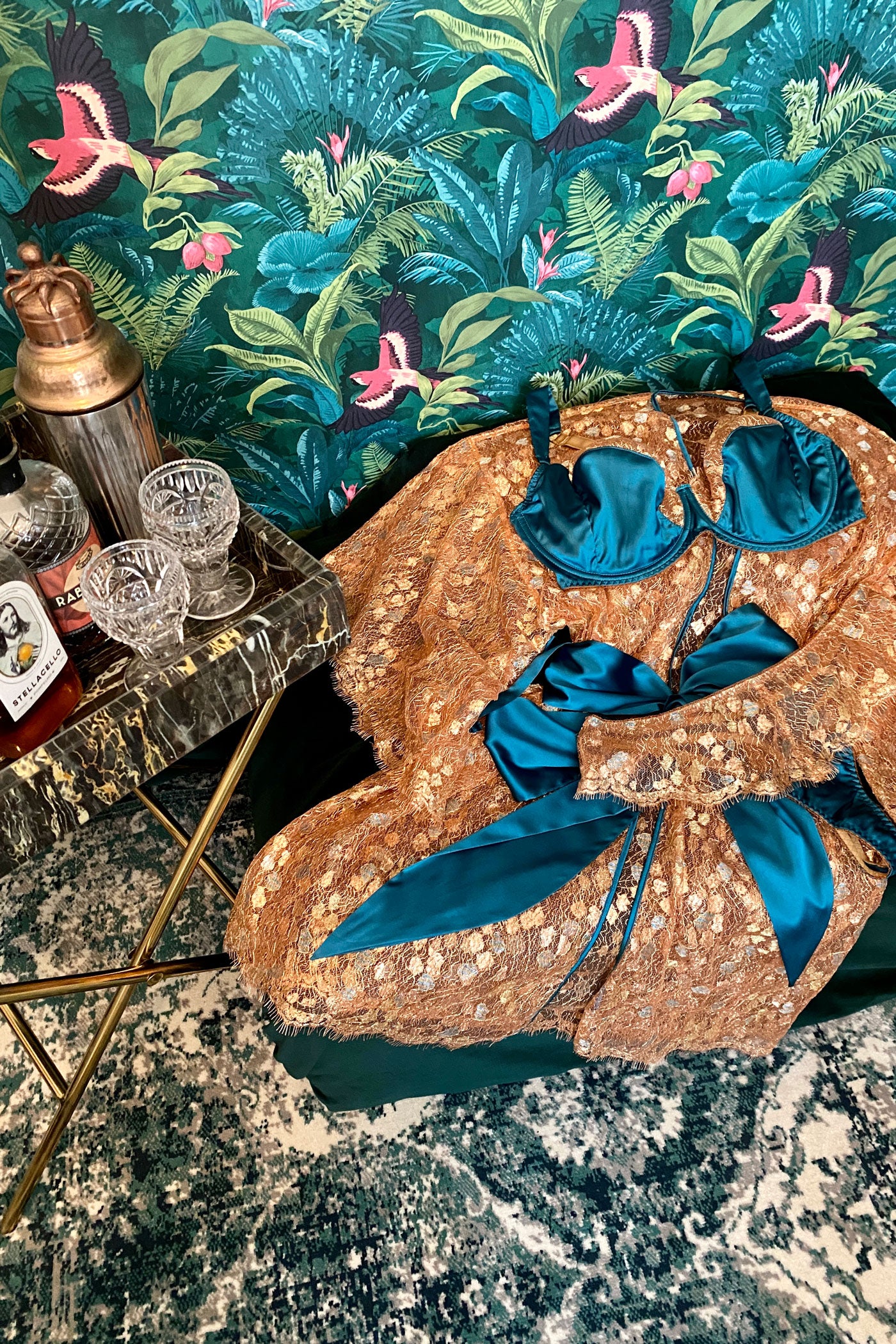 Gold lace robe with matching bra and thong flatlay with lush wallpaper and cocktails