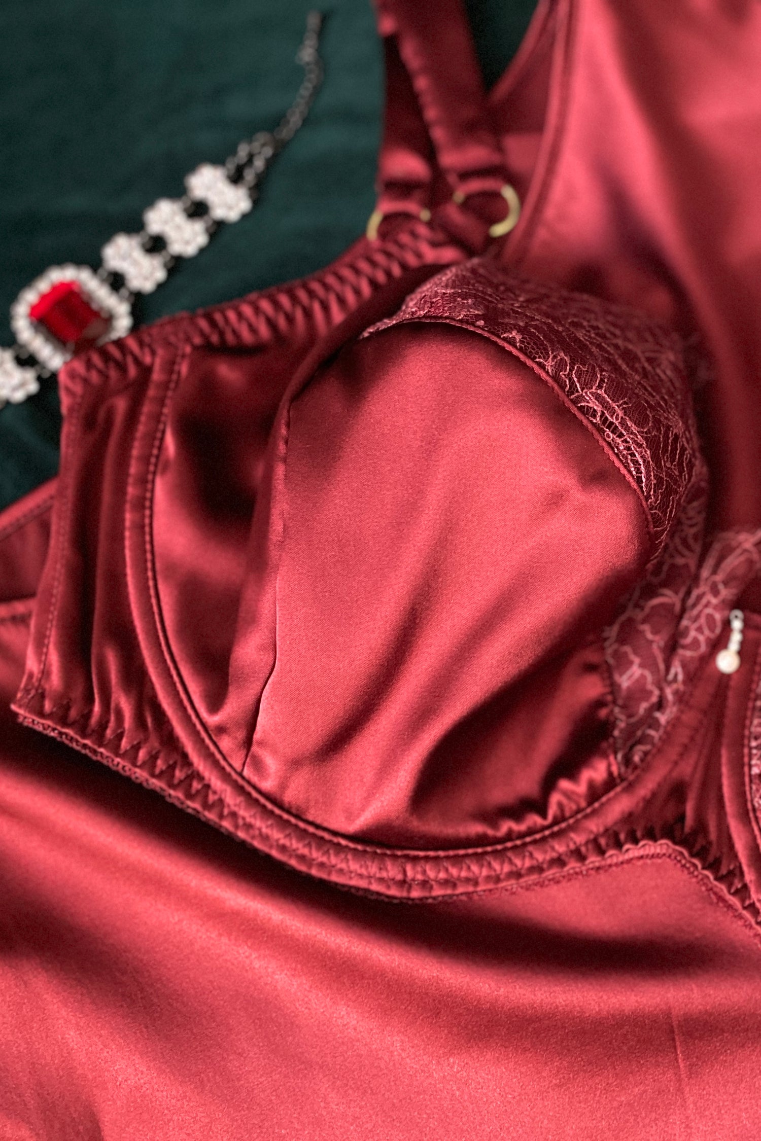 Close up of dark red silk bra cup, with matching red lace top cup and gold ring adjusters