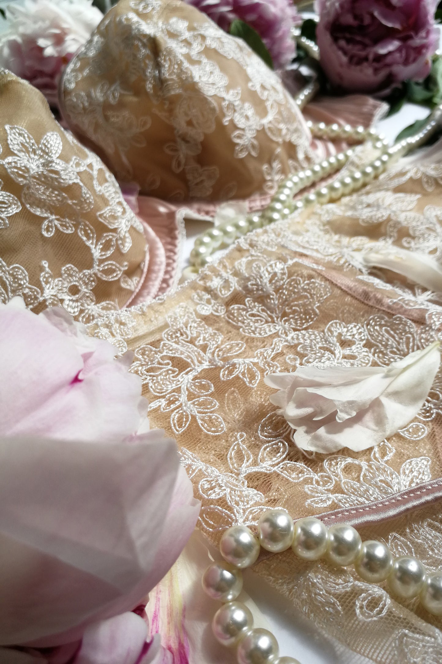Flatlay detail of sheer embroidery and pink silk binding on bra and garter belt