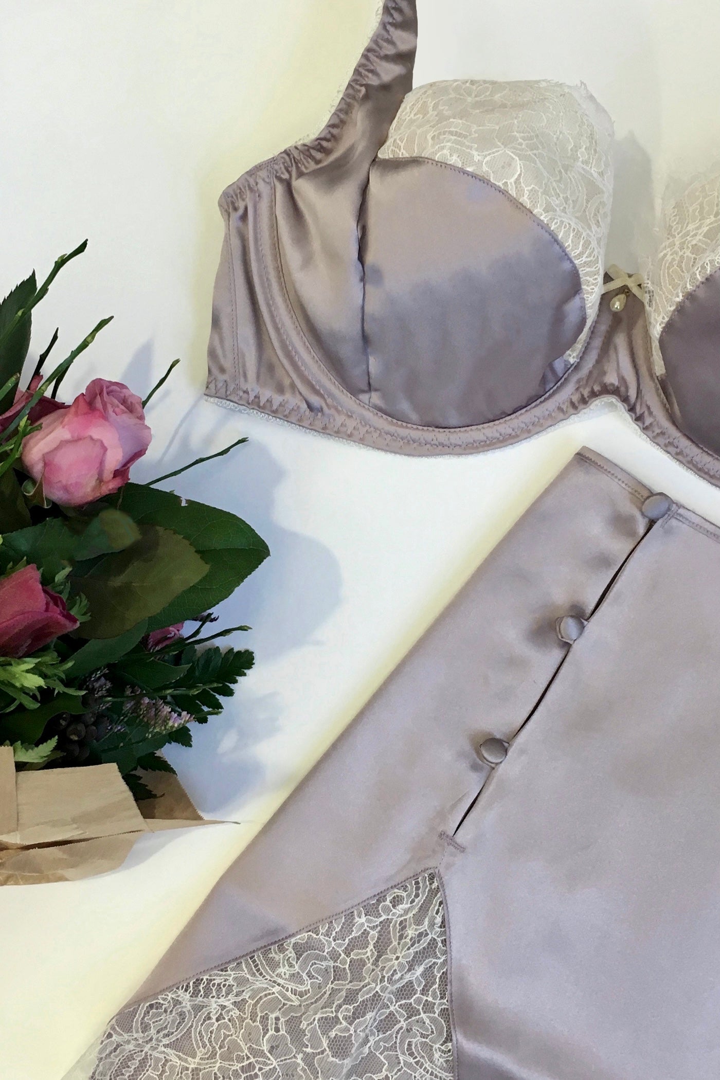 Flatlay of vintage style lingerie set in purple silk and white lace with button detail on tap pants